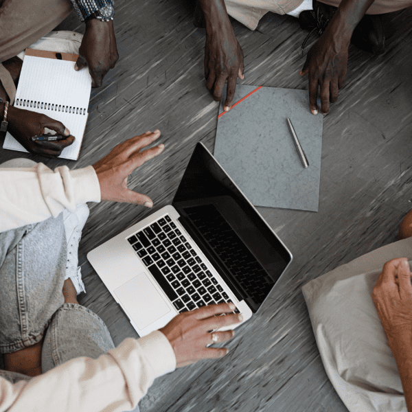 Jeunes assis en rond qui discutent avec sur le sol, un ordinateur et des stylos