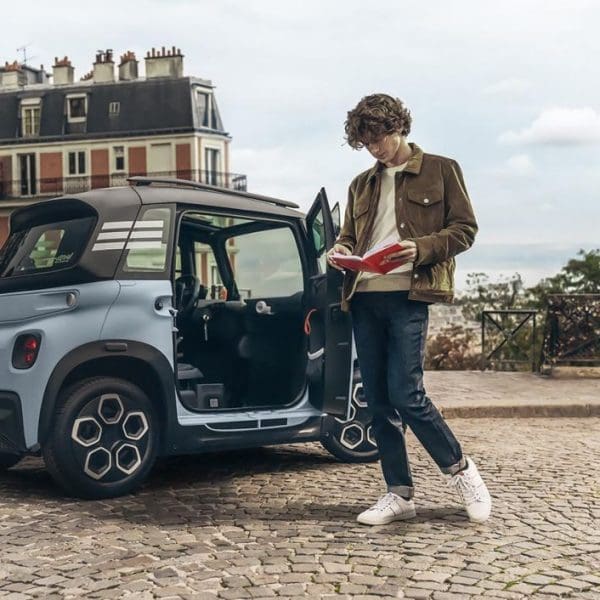 voiture sans permis sur des pavés avec un homme qui lit un livre à côté de la voiture