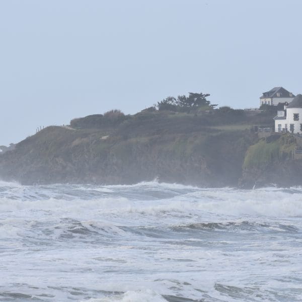 vagues qui s'éclatent contre une falaise avec une maison au bord.