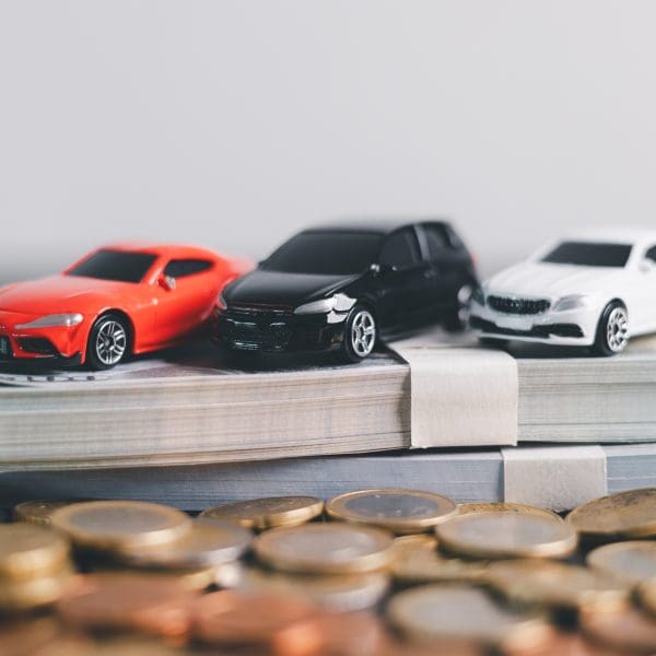 3 petites voitures posées sur des billets et devant les billets se trouvent des pièces qui représentent les économies