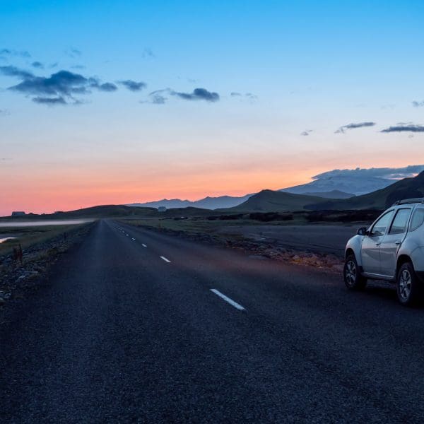 voiture sur la route face à un coucher de soleil avec les nuages et les montagnes à l'horizon