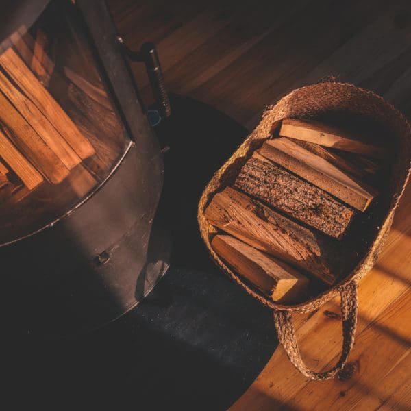 Vue de haut en bas d’un intérieur confortable avec un poêle à bois noir et un panier en osier rempli de bois de chauffage, éclairé par la douce lumière du soleil du soir