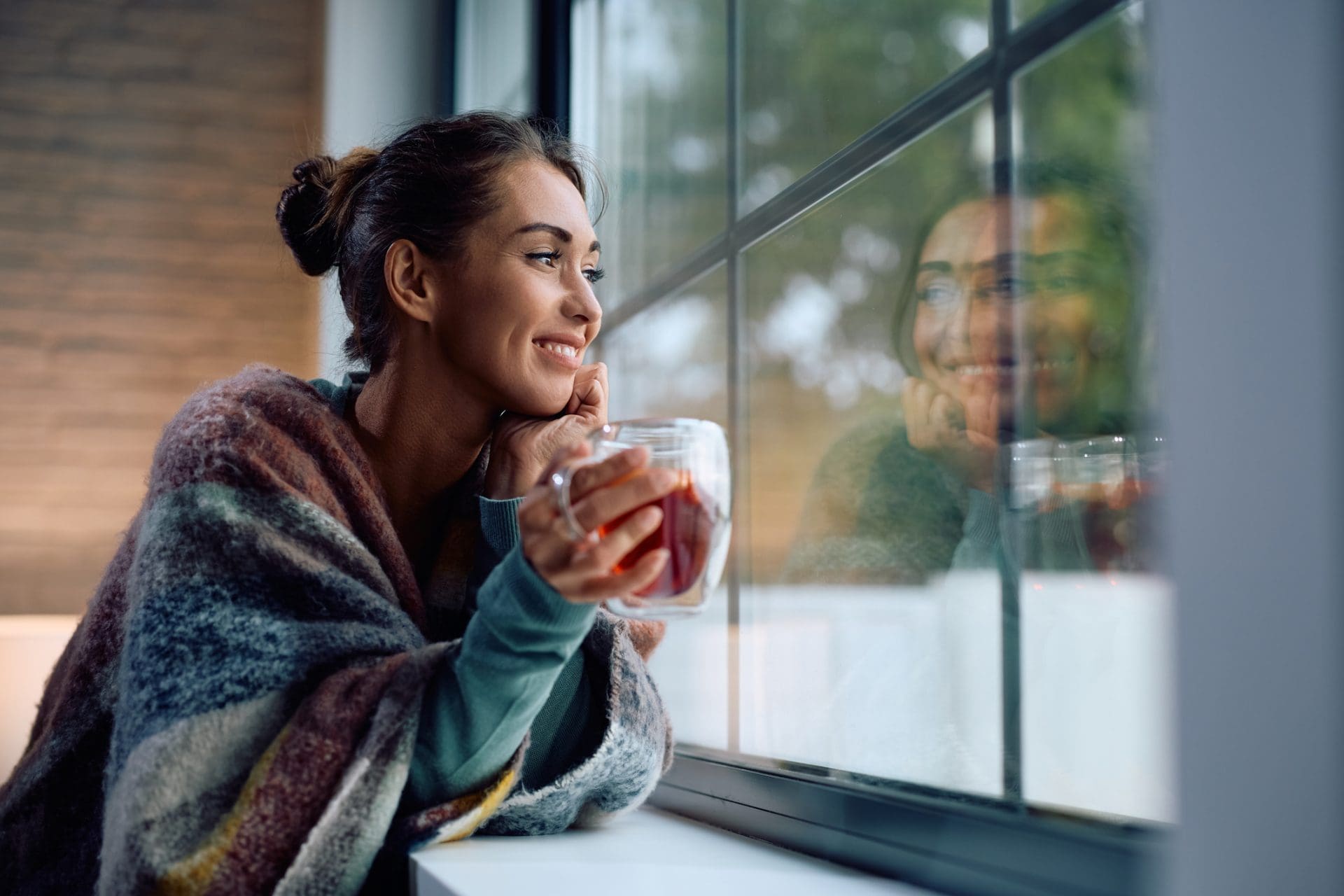 Femme souriante rêvant tout en buvant du thé chaud à la maison