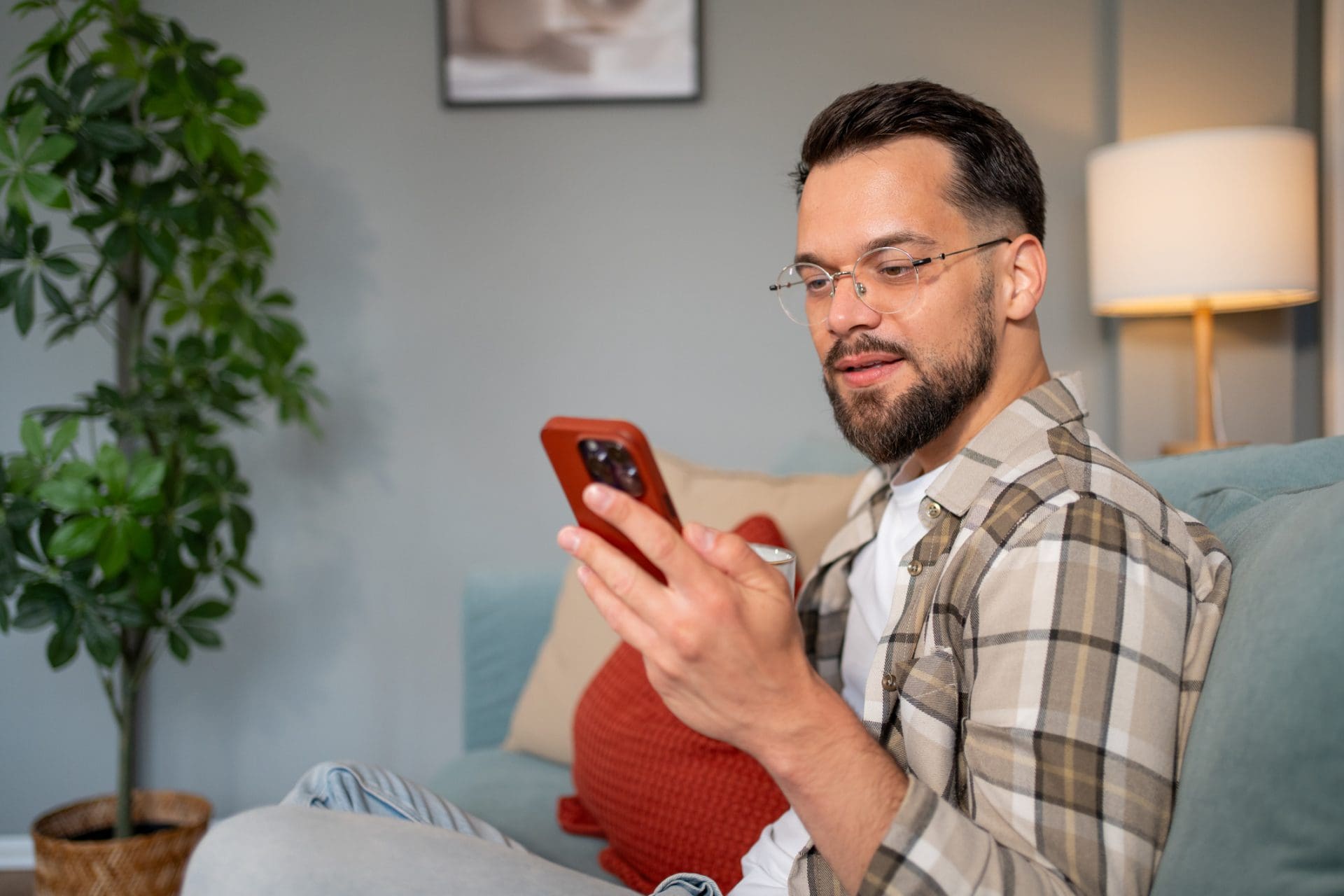Jeune homme se relaxant sur le canapé à l’aide d’un smartphone et buvant du café 